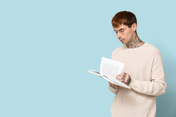 Young tattooed man reading book on blue background