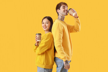 Young couple with cups of coffee on yellow background