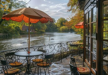 Obraz premium A charming riverside café with wrought-iron furniture, colorful parasols, and a view of a gently flowing river with swans gliding by. The peaceful setting invites relaxation.