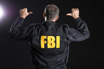 Mature FBI agent pointing at himself on black background, back view