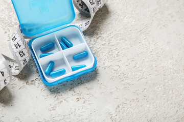 Container with weight loss pills and measuring tape on grey grunge background