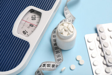 Bottle with weight loss pills, scales and measuring tape on blue background