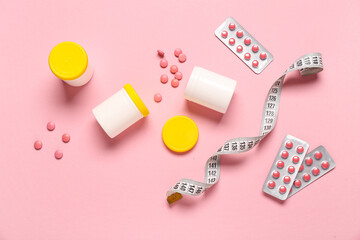 Bottles, blister packs with weight loss pills and measuring tape on pink background