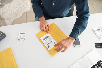 Male online store seller packing envelope for client at table in warehouse, top view