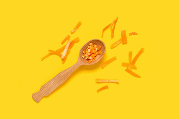 Composition with wooden spoon and orange peel on yellow background