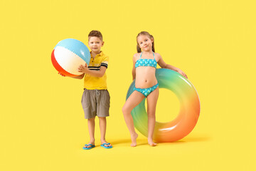 Cute little children with beach ball and inflatable ring on yellow background
