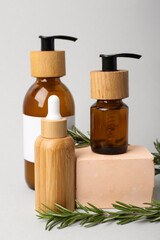 Bottles of cosmetic products and fresh rosemary on light background