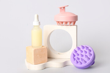 Stands with hair scalp massagers and bottle of cosmetic product on grey background