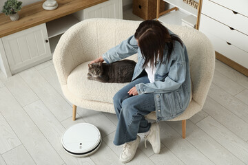 Young woman with cute cat and modern robot vacuum cleaner at home