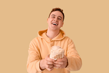 Young happy man smiling and holding doner kebab on beige background
