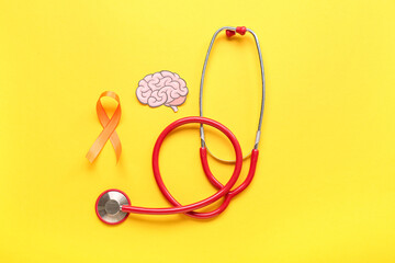 Paper brain with stethoscope and orange ribbon on yellow background. Multiple Sclerosis Awareness...