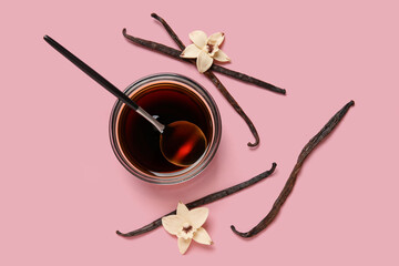 Vanilla extract in bowl with spoon, vanilla pods and flowers on pink background. Top view