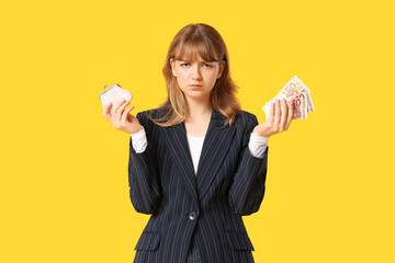 Sad young woman holding pink purse and money on yellow background