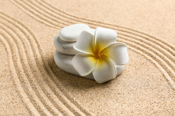 Stack of spa stones and plumeria on sand with lines. Zen concept