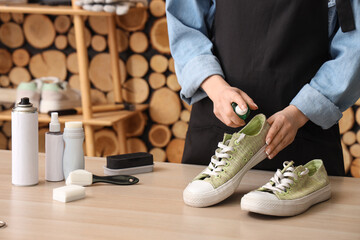 Female shoemaker with stylish gumshoes and cleaning supplies at wooden table, closeup