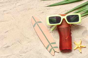 Composition with bottle of sunscreen cream, sunglasses and decor on sand