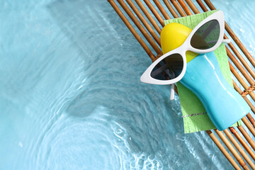 Bamboo mat with bottle of sunscreen cream and sunglasses near swimming pool