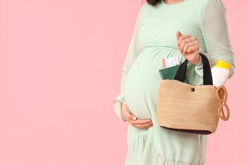 Young pregnant woman holding bag with passport and sunscreen on pink background. Travel concept