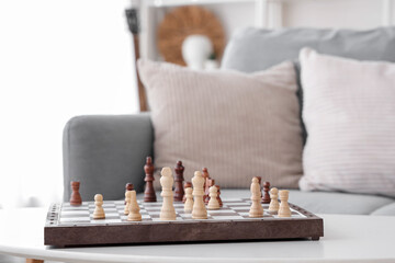 Game board with chess pieces on coffee table near sofa in living room, closeup