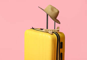 Yellow suitcase with toy airplane and wicker hat on pink background. Travel concept