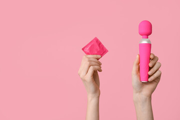 Female hands with vibrator and condom on pink background, closeup