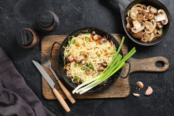 Frying pans with tasty pasta, mushrooms and spices on wooden background