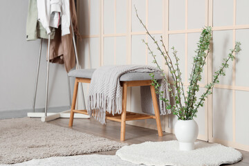 Soft bench, white rug and vase with blossoming branches in stylish room