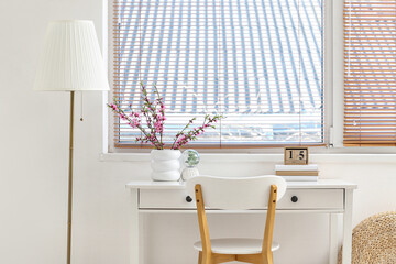 Vase with Sakura blooming branches on stylish workplace in white room