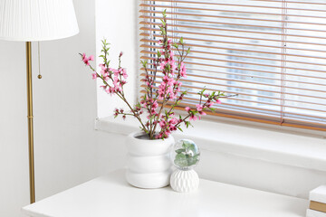 Vase with Sakura blooming branches on table in white room