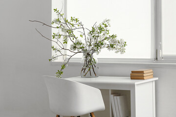 Vase with blooming branches on workplace in white room