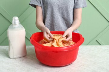 Woman washing clothes in plastic basin on table against green background