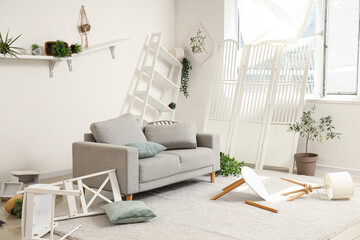 Interior of messy living room with sofa, shelves and plants