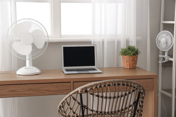 Comfortable workspace with modern laptop and electric fan on wooden desk at home office