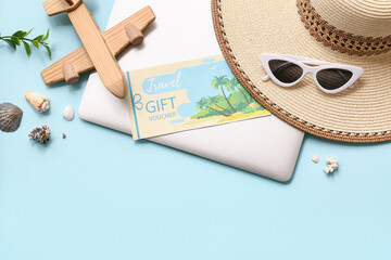 Composition with travel gift voucher, beach accessories and modern laptop on color background