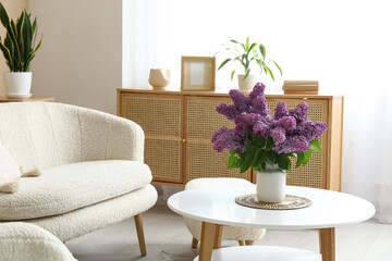Stylish interior of living room with bouquet of lilacs branches on coffee table near white sofa