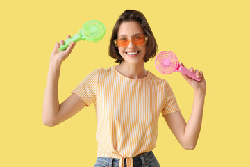 Young woman with two small electric fans on yellow background