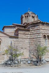 A historical Byzantine church with stone walls, small windows and domes, surrounded by trees under a clear blue sky, in Athens, Greece
