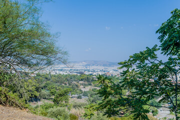 A distant city seen from a scenic viewpoint, with trees and greenery in the foreground, in Athens, Greece