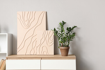 Stylish paintings with plant on commode in light room