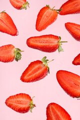 Flying halves of sweet strawberries on pink background
