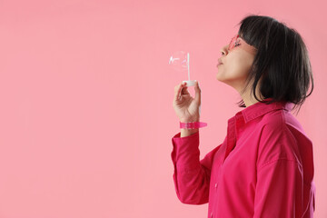 Young woman blowing soap bubbles on pink background - Powered by Adobe