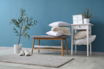 Cozy bench, houseplant, pillow and coffee table near blue wall in stylish room, blurred view