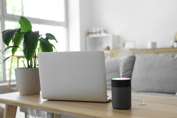 Air humidifier with laptop and plant on table in living room, closeup