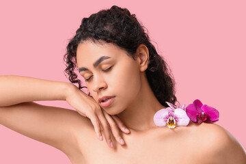 Beautiful young African-American woman with orchid flowers on pink background