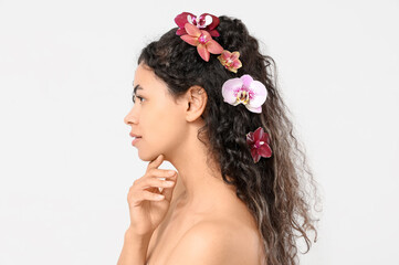 Beautiful young African-American woman with orchid flowers in her hair on white background