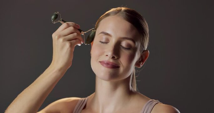 Smile, skincare and woman with jade roller for natural beauty, massage and luxury cosmetics in studio. Dermatology, facial care and girl with confidence, gua sha and healthy skin on grey background.