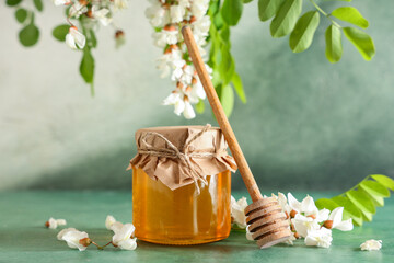 Jar of sweet honey with acacia flowers and dipper on green table