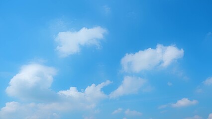 A bright blue sky dotted with fluffy white clouds. The vibrant blue backdrop and soft, scattered clouds create a tranquil and cheerful atmosphere, typical of a clear, sunny day. Blue sky background.
