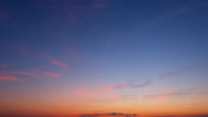A serene sunrise with a gradient sky transitioning from deep blue at the top to warm orange near the horizon. Light pink clouds are scattered across the sky, adding to the tranquil atmosphere.
