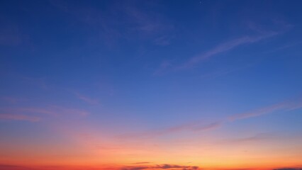 A beautiful sunrise with a clear sky transitioning from deep blue at the top to vibrant orange at the horizon. Light pink clouds are scattered across the sky, enhancing the tranquil scene.
